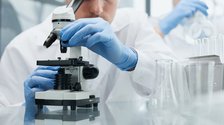 Young scientist or researcher in protective workwear studying new virus in microscope to develop antidote for fighting coronavirusの写真素材