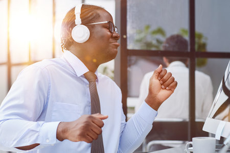 a man at a workplace at a table in front of a computer with headphones listening to musicの写真素材