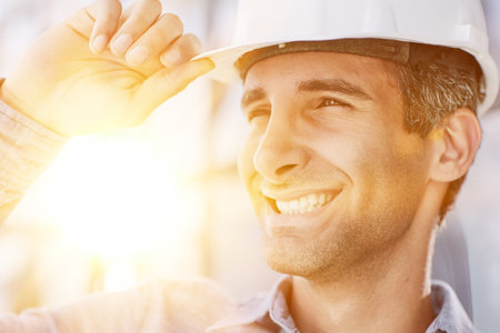 Smiling young unshaven business man in light shirt protective construction helmet.の写真素材