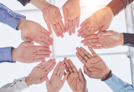 young volunteers putting their hands on top of each other like a real team while standing in charitable organization officeの写真素材