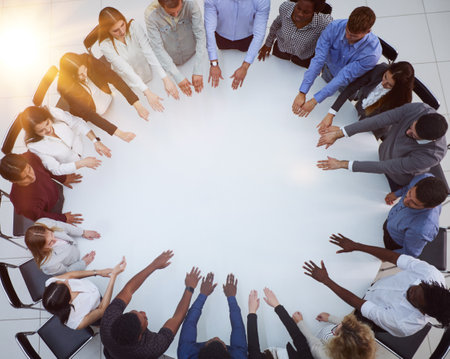 a large group of people sitting at a round table with their arms outstretchedの写真素材