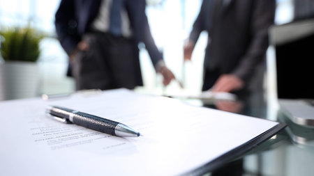 Two men are sitting at a desk with a pen and a piece of paper. Scene is serious and focusedの写真素材
