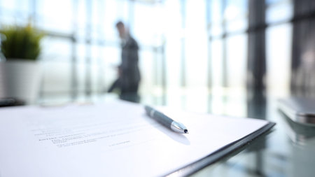 A man is walking past a desk with a pen and a piece of paper. The man is wearing a suit and he is in a hurry. The pen is on the paper, which is open to a blank pageの写真素材