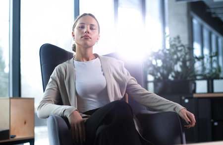 A woman is sitting in a chair in a room with a potted plantの写真素材