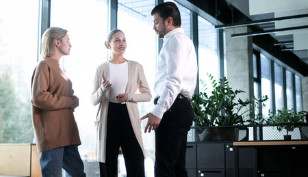 Three people are standing in a room, one of them is wearing a brown sweaterの写真素材