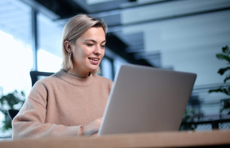 A woman is sitting at a desk with a laptop in front of herの写真素材