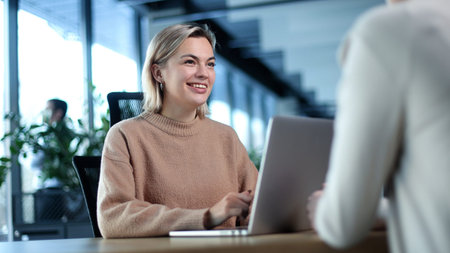 A woman is sitting at a desk with a laptop in front of herの写真素材