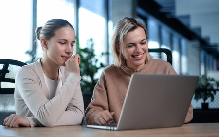 Two women are sitting at a table looking at a laptopの写真素材