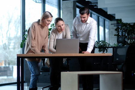 Three people standing in a room with a laptop on a deskの写真素材