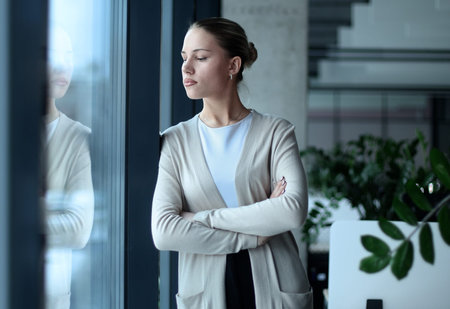 A woman in a business suit stands in front of a windowの写真素材