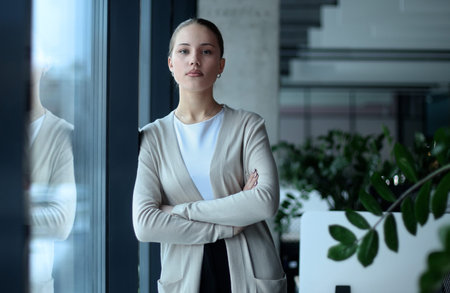 A woman in a business suit stands in front of a window with her arms crossedの写真素材