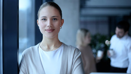 A woman is standing in front of a window with her arms crossed