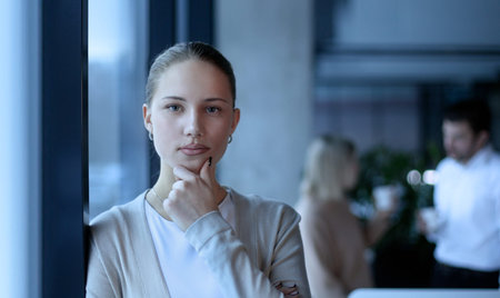 A woman is standing in front of a window with her hand on her chin