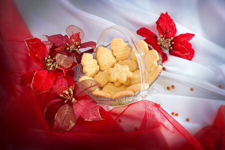 Variety shaped christmas butter cookies on cristal serving bowl and red-gold christmas leaves on white satin and red chiffon draperyの写真素材