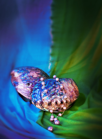 Paua shell and pearl ornaments on blue drapery, Paua shell pearl ear ring and pearl necklace on blue backgroundの写真素材
