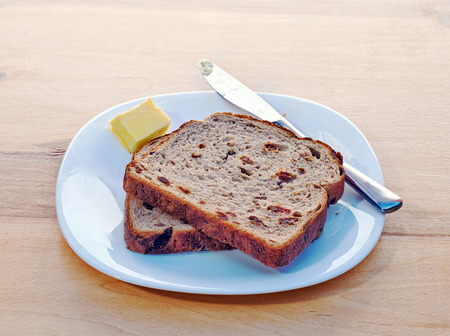Raisin toast, butter, stainless knife and ceramic plate placed on wooden tableの写真素材