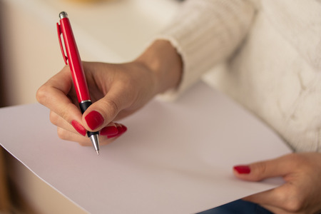 Female hands with red nails write on a sheet of paperの写真素材