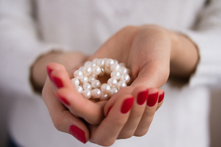 Pearls in female hands with red manicureの写真素材