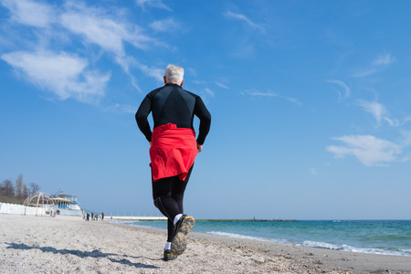 Gray-haired man runs along the beach tracksuitの写真素材