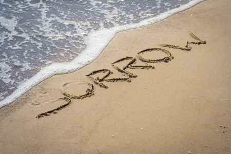 inscription sorrow on beach sand near the water. word written on a diagonal and a little blurry...