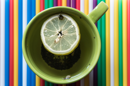 Green cup of tea with lemon on a bright colored striped backgroundの写真素材