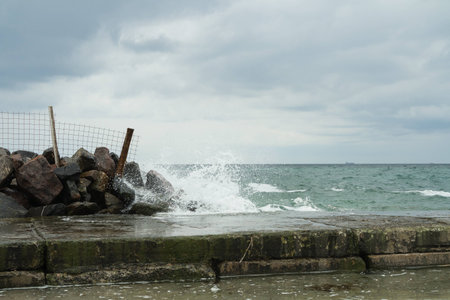 Waves breaking on rocks near the pier in cloudy weatherの写真素材