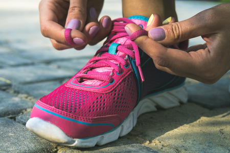 Hands of a young woman lacing bright pink and blue sneakers. Shoes standing on the pavement of stones and sand. In female hands purpleyellow manicure. Photographed closeup.の写真素材