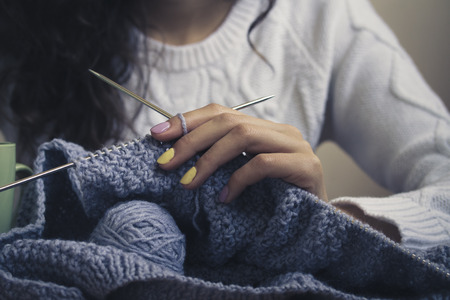 In the center of the image of a young girl39s hand with bright manicure keeps knitting with spokes. The girl wearing a white sweater. Vintage photo. Closeup.の写真素材