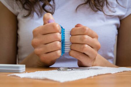 Girl in white t-shirt sitting at the table and makes a manicure brush nail. On the wooden table are nail scissors and a paper towel.の写真素材