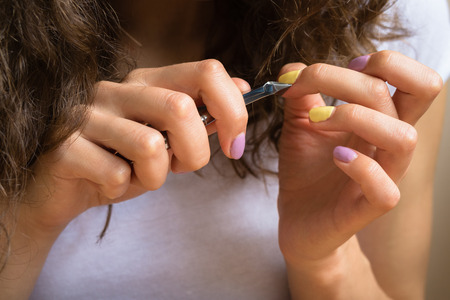 Care for cuticles with manicure scissors. Female hands with a bright manicure keep cosmetic tool closeup.の写真素材