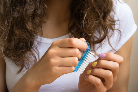 Treatment of the nails with a brush. Hands of a young girl with a bright manicure keep cosmetic tool closeup.