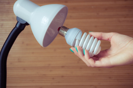 Installation of a modern economical bulb in a table lamp. Female hand holding spiral lamp.