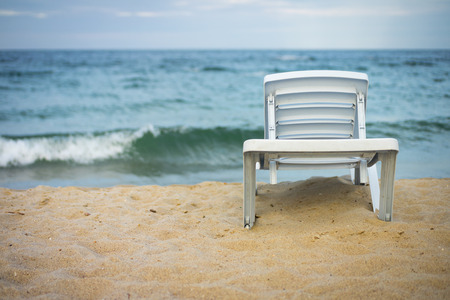 Plastic white lounge chair on empty beach.  
The sunbed stands on the sand near the water.の写真素材