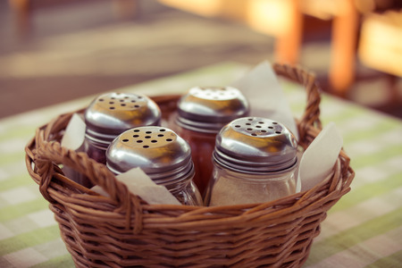 Spices in glass bottles in a wicker basket on the table in cafe. Lunch outdoors on a summer day. Image with instagram filter. Soft focus.の写真素材