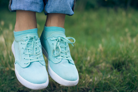 Female legs in jeans and sport shoe floating in the air above the green grass in the park. Flying sneakers outdoors. Conceptual image.の写真素材