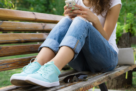 Girl in jeans sits on a park bench and using a mobile phoneの写真素材