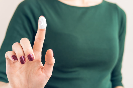 Woman in a green T-shirt and a maroon manicure shows hand cream on fingerの写真素材