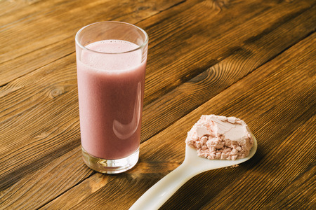 Sports protein on the spoon and in a glass Cup on wooden backgroundの写真素材