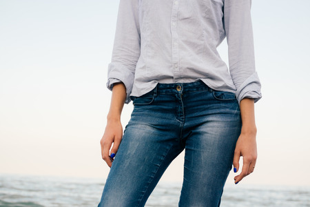 Details of women's clothing. A woman in a striped shirt and blue jeans standing on sea background.の写真素材