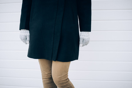 Girl in black coat, beige jeans and gray gloves standing on white background. Details of women's...