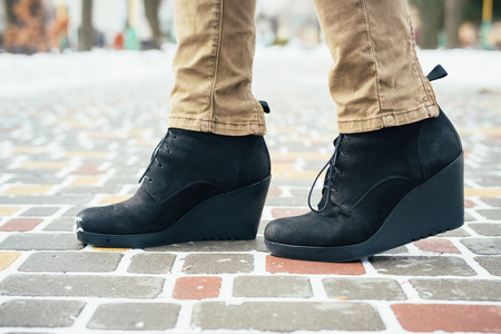 Female feet in black boots standing on the sidewalk in the winter, close-upの写真素材