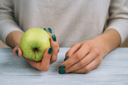 Female hands holding green apple. Woman sits at the kitchen table close-up.の写真素材