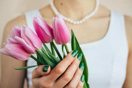 Beautiful woman in white dress and pearl necklace holding a pink tulips, close-upの写真素材