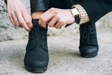 Woman in elegant clothes tying shoelaces on shoes close up. Shoelaces untied during a walk in the...