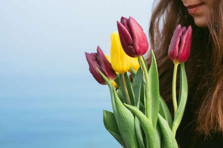 Girl holds a bouquet of bright tulips on the background of blue seaの写真素材