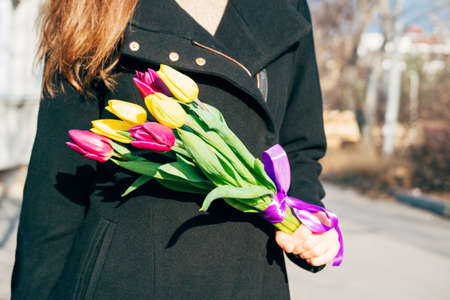 Woman in black coat holding a bright bouquet of flowers on a sunny dayの写真素材