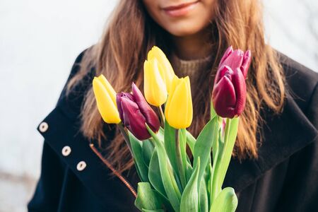 Smiling girl holds a bouquet of bright tulips outdoors, close-upの写真素材