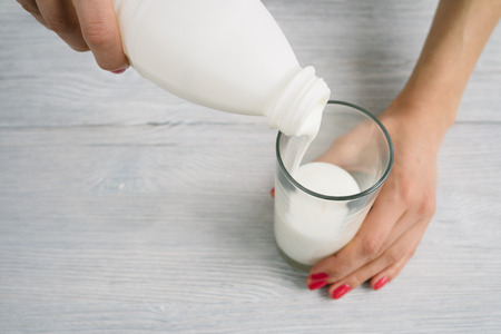 Female hands with a red manicure pour yoghurt into a glass. Shallow depth of field, top view.の写真素材