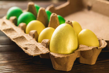 Open packing with hand painted eggs. Yellow and green Easter eggs on a wooden table.の写真素材
