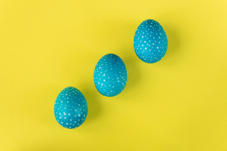 Three blue Easter eggs on bright yellow background, top viewの写真素材